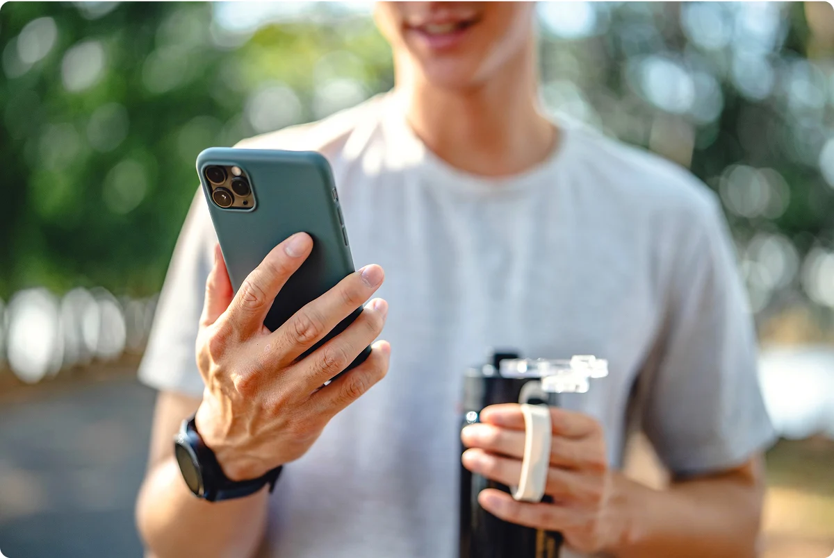 un chico joven mirando su móvil mientras sostiene una botella de  agua en la otra mano