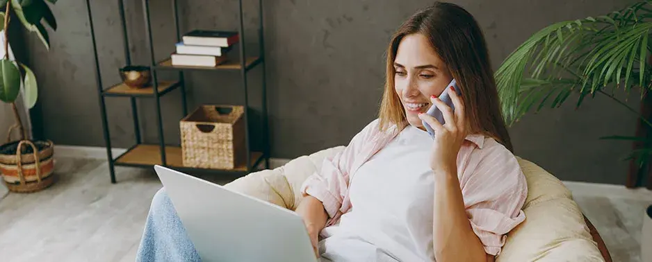 Mujer hablando por teléfono en un sofá y con portátil